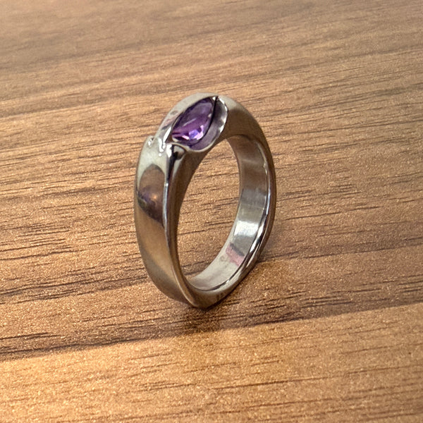 Silver ring with a purple gemstone on a wooden surface